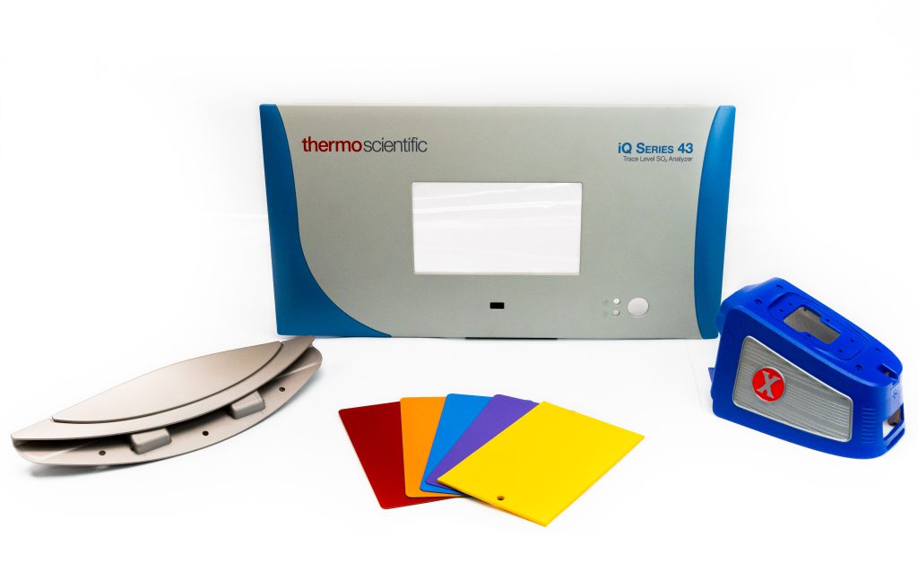 Array of cosmetic coating related parts/swatches. On the ThermoScientific part: we spray the blue and do the inkjet printing to denote which type of analyzer it is. At far left: JetAvoin part; we do some electromechanical assembly on these as well as cosmetic coats. At far right: The part is entirely gray to start and we apply the blue and red.